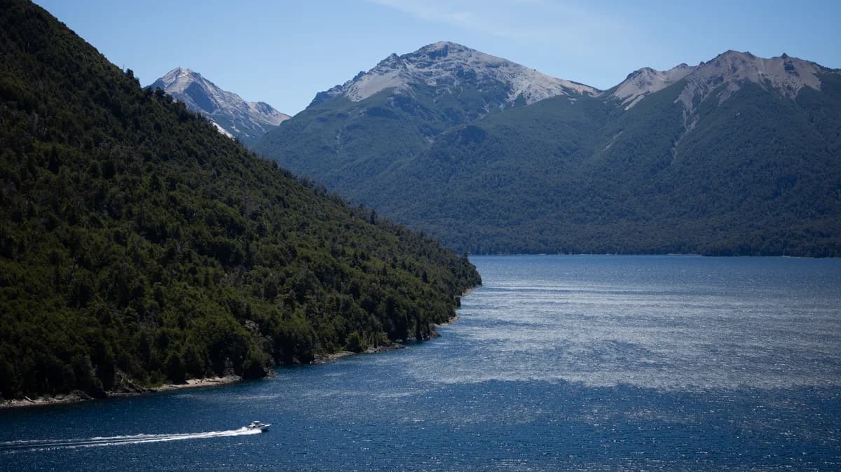 Boat cruising at high speed on a lake's branch, next to a mountain, and with big mountains in the background