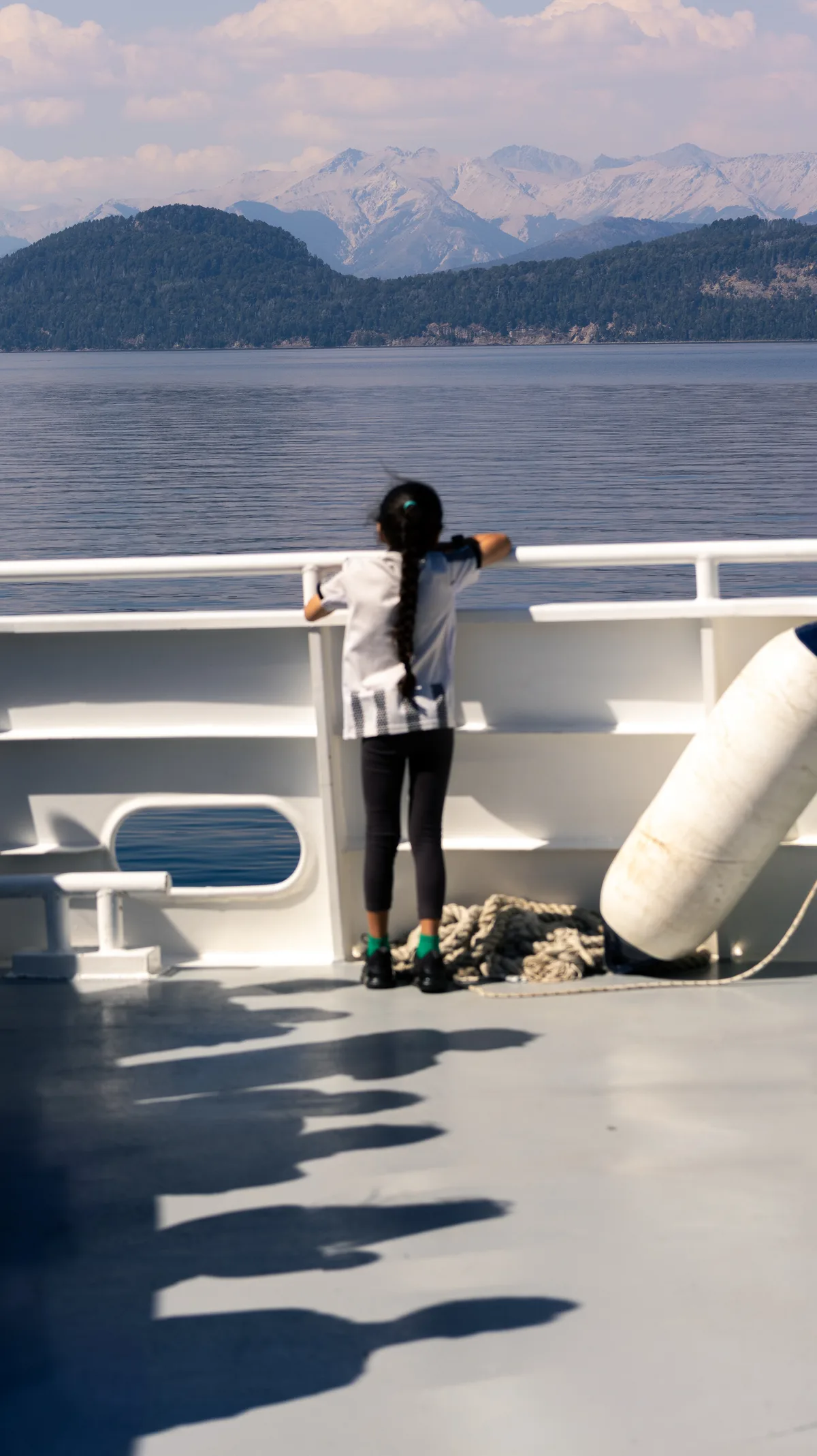 Girl watching lake and mountains over a ferry's handrail