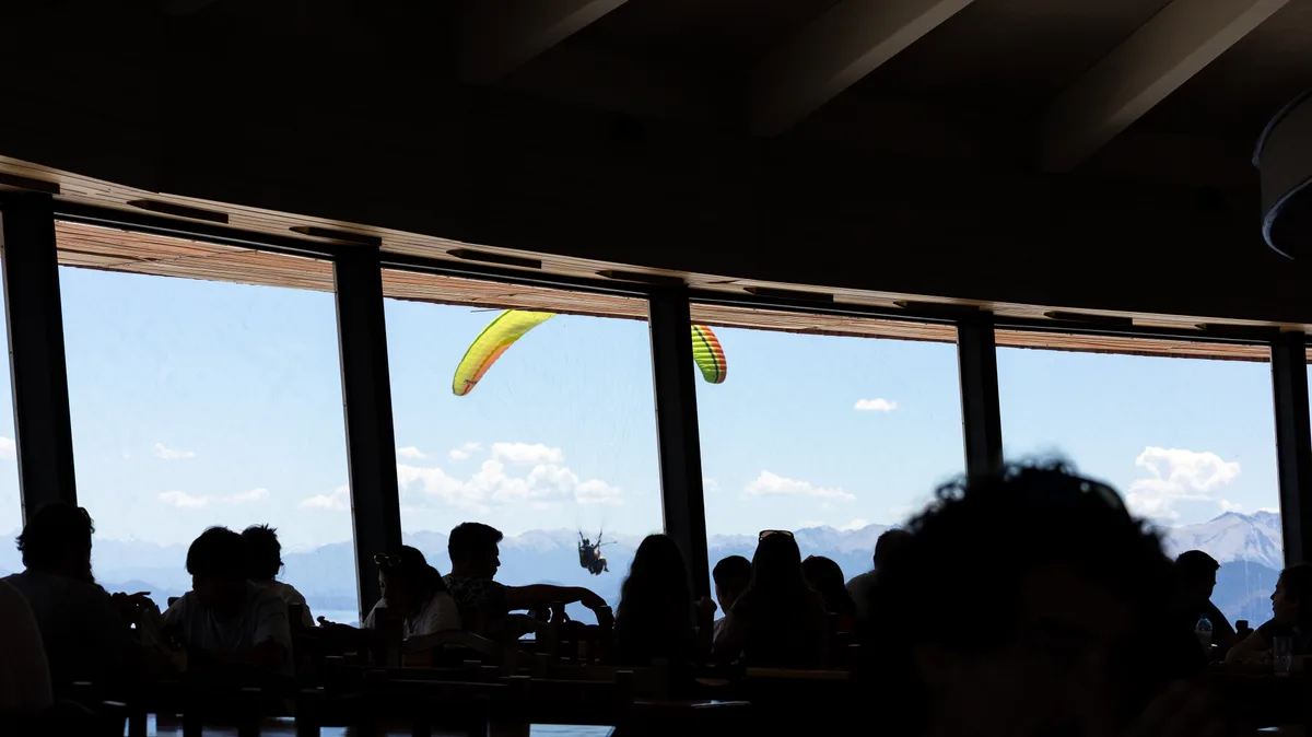 Paraglider flying by a window at Cerro Otto's bar, Bariloche