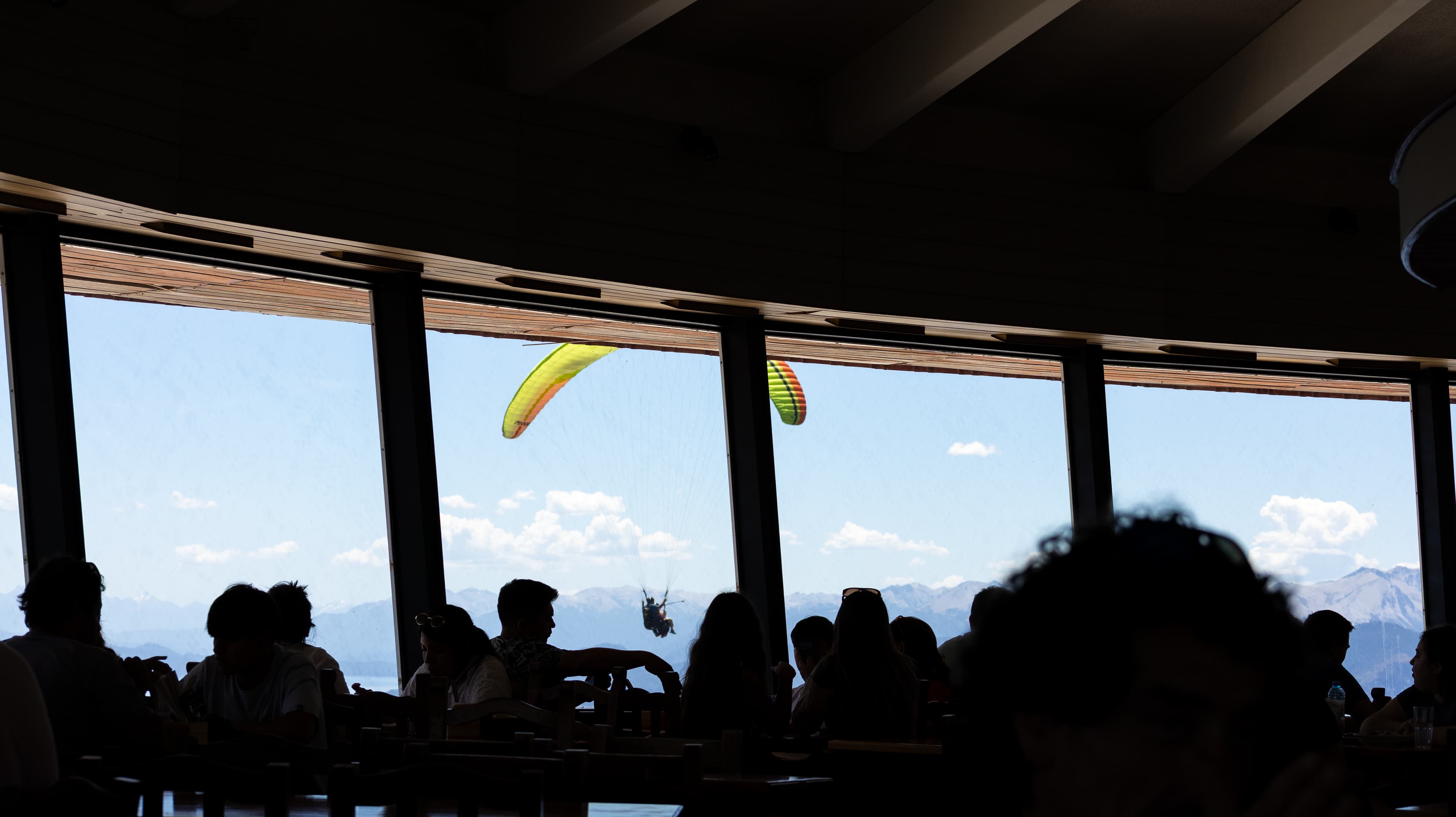 Paraglider flying by a window at Cerro Otto's bar, Bariloche