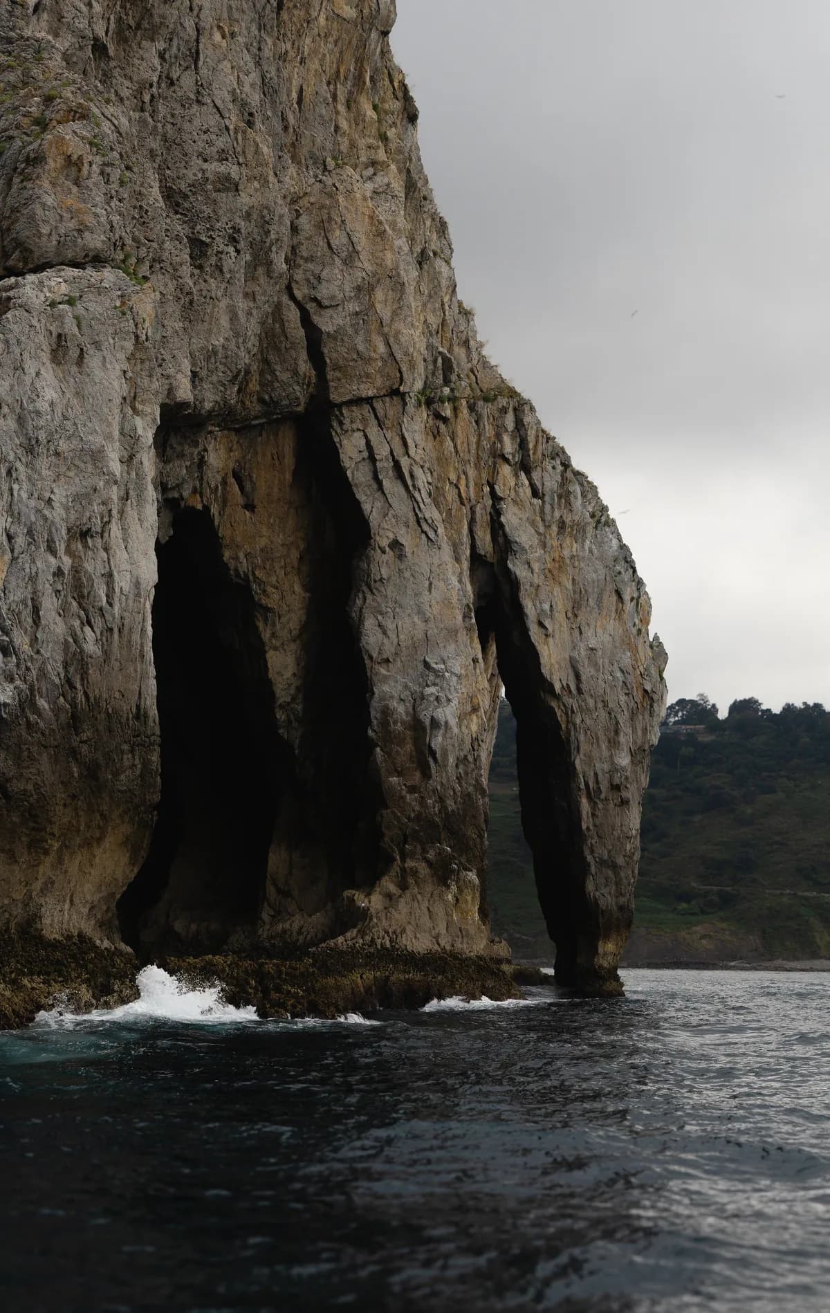 Waves break at the base of a towering rock formation carved with a natural arch and sea caves