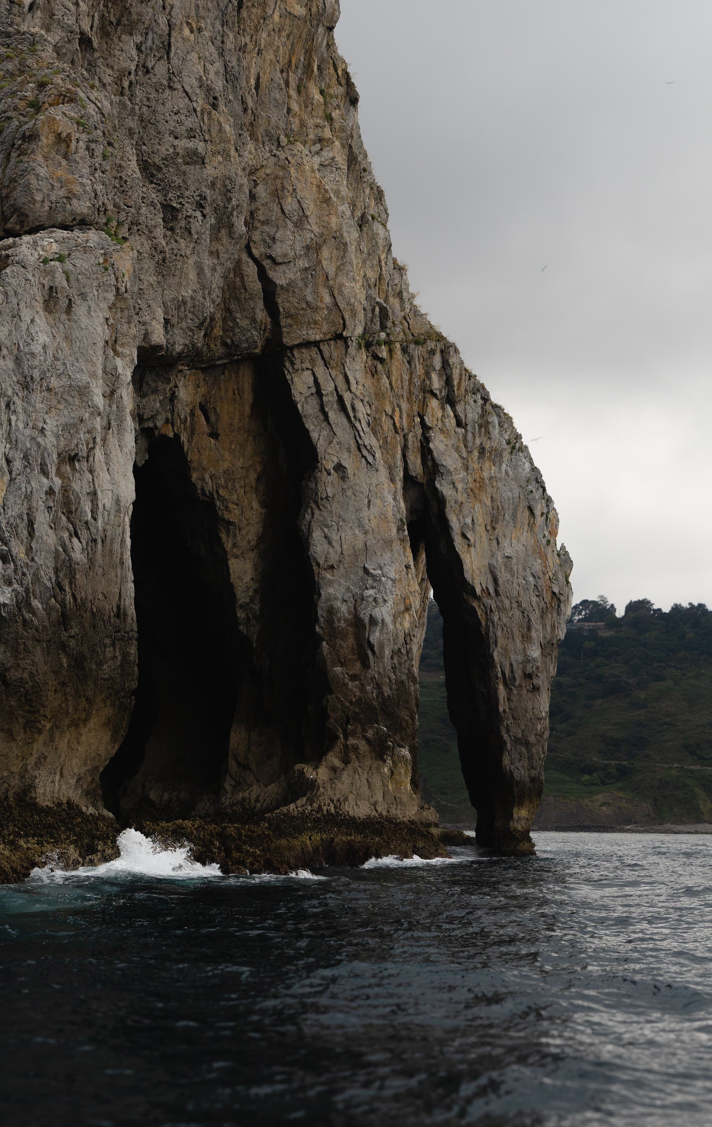 Waves break at the base of a towering rock formation carved with a natural arch and sea caves