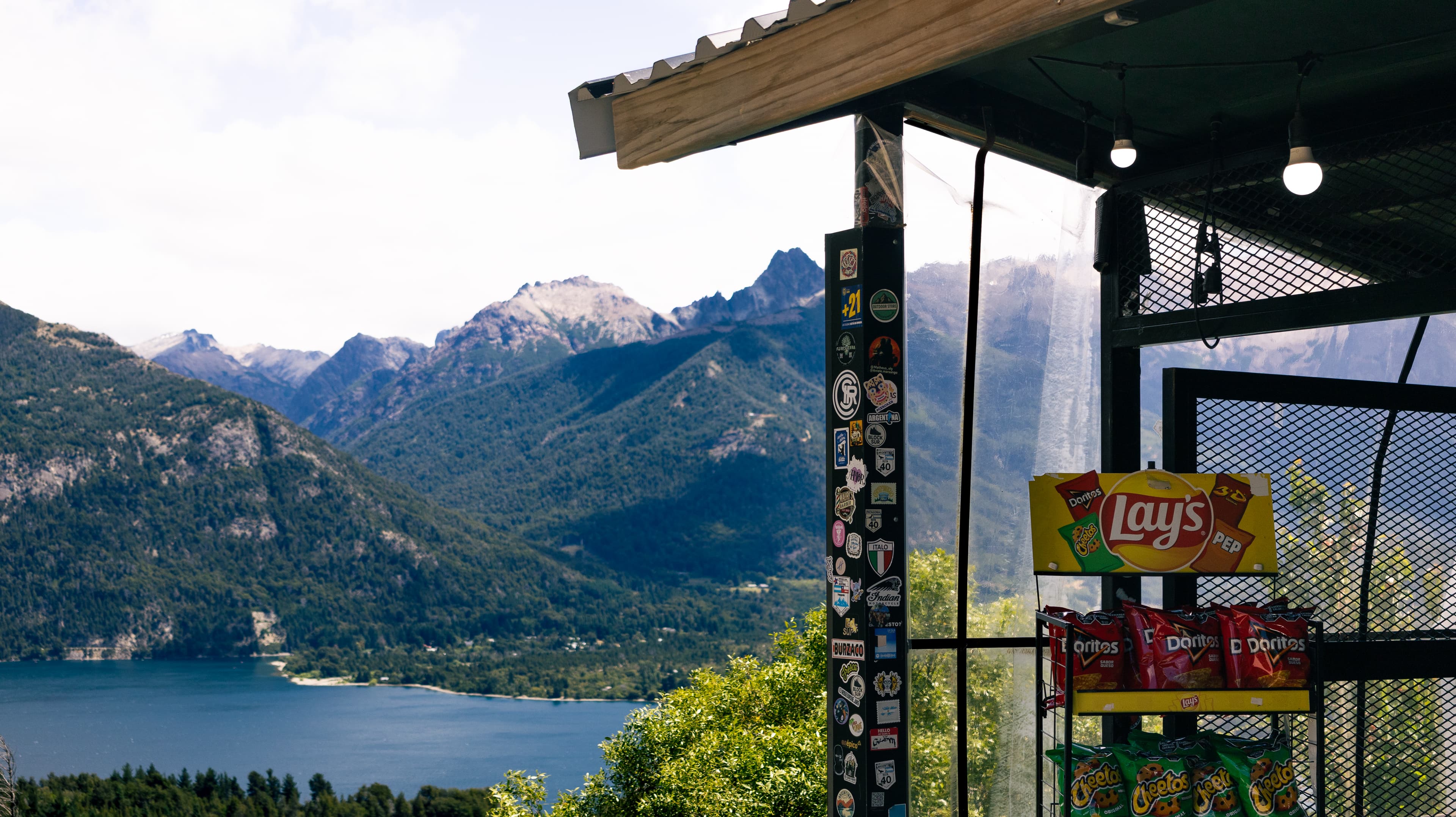 A stand selling unhealthy chips and snacks with a pristine lake and mountains in the background